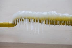 Frozen plumbing pipe covered in thick ice and hanging icicles, showing the effects of freezing temperatures.
